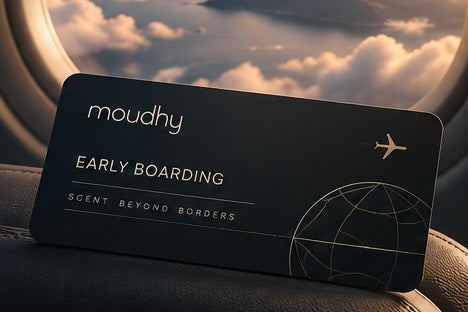 A centred Moudhy Early Boarding pass beside an aircraft window at sunset.